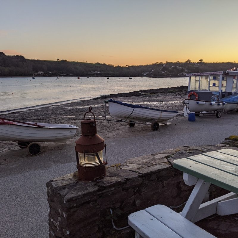 A view of Helford Passage Beach with a bench, lantern and boats